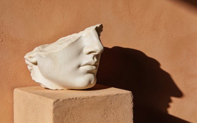 Pale plaster face fragment in profile against a warm ochre wall