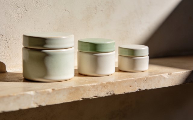 Three cream ceramic jars on a warm stone shelf