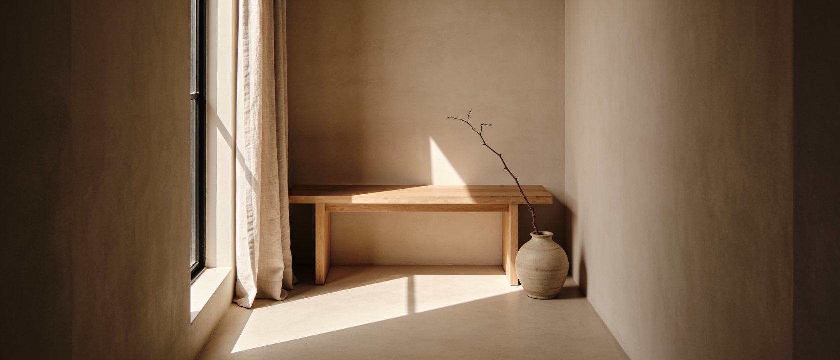 A timber bench beside a linen curtain in a quiet clinic hallway, afternoon light pooling on the floor