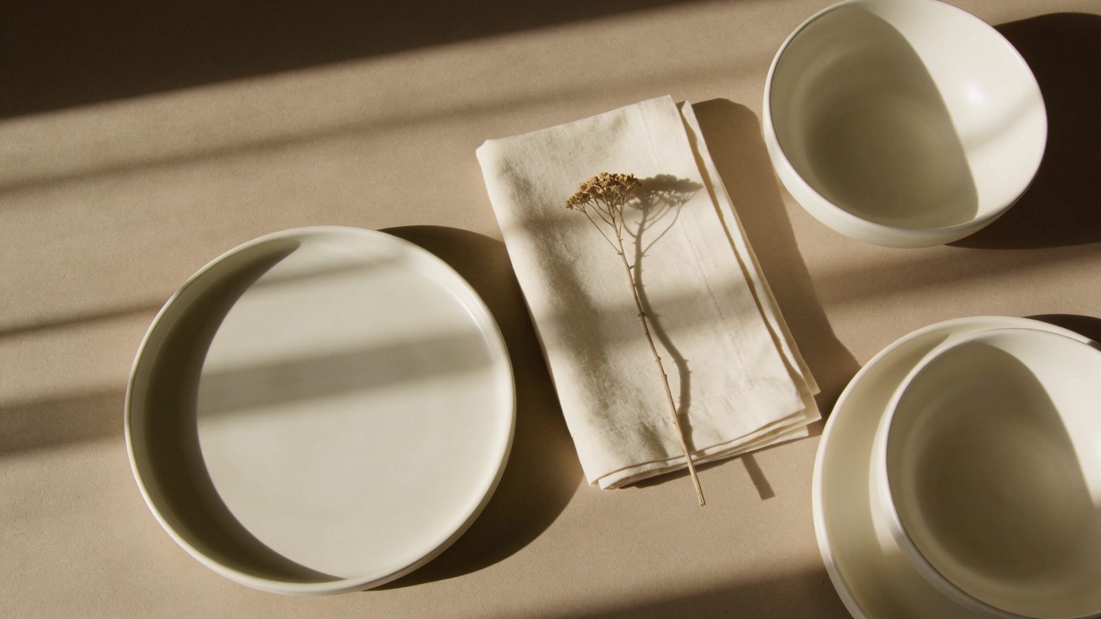 Overhead arrangement of ceramic dishes, cream linen and a dried botanical stem